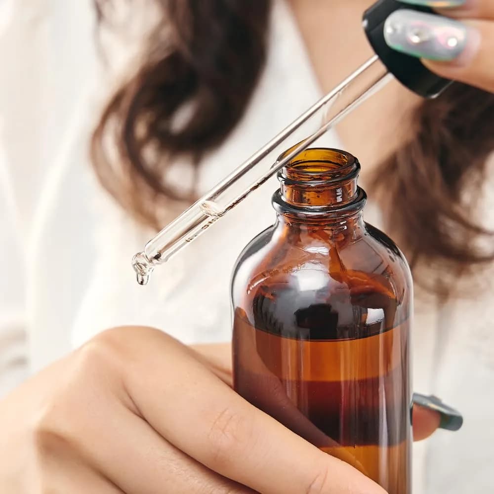 A dropper of concentrated formulation liquid held above an amber glass bottle